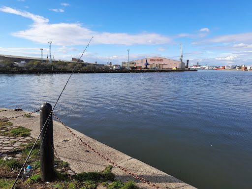 An angler fishing on the banks of the River Mersey with the Liverpool skyline in the background.